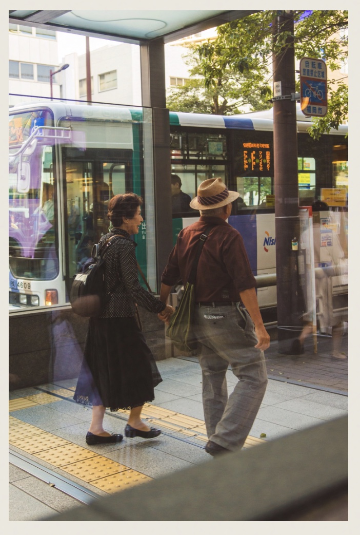 An older couple holding hands at a bus stop